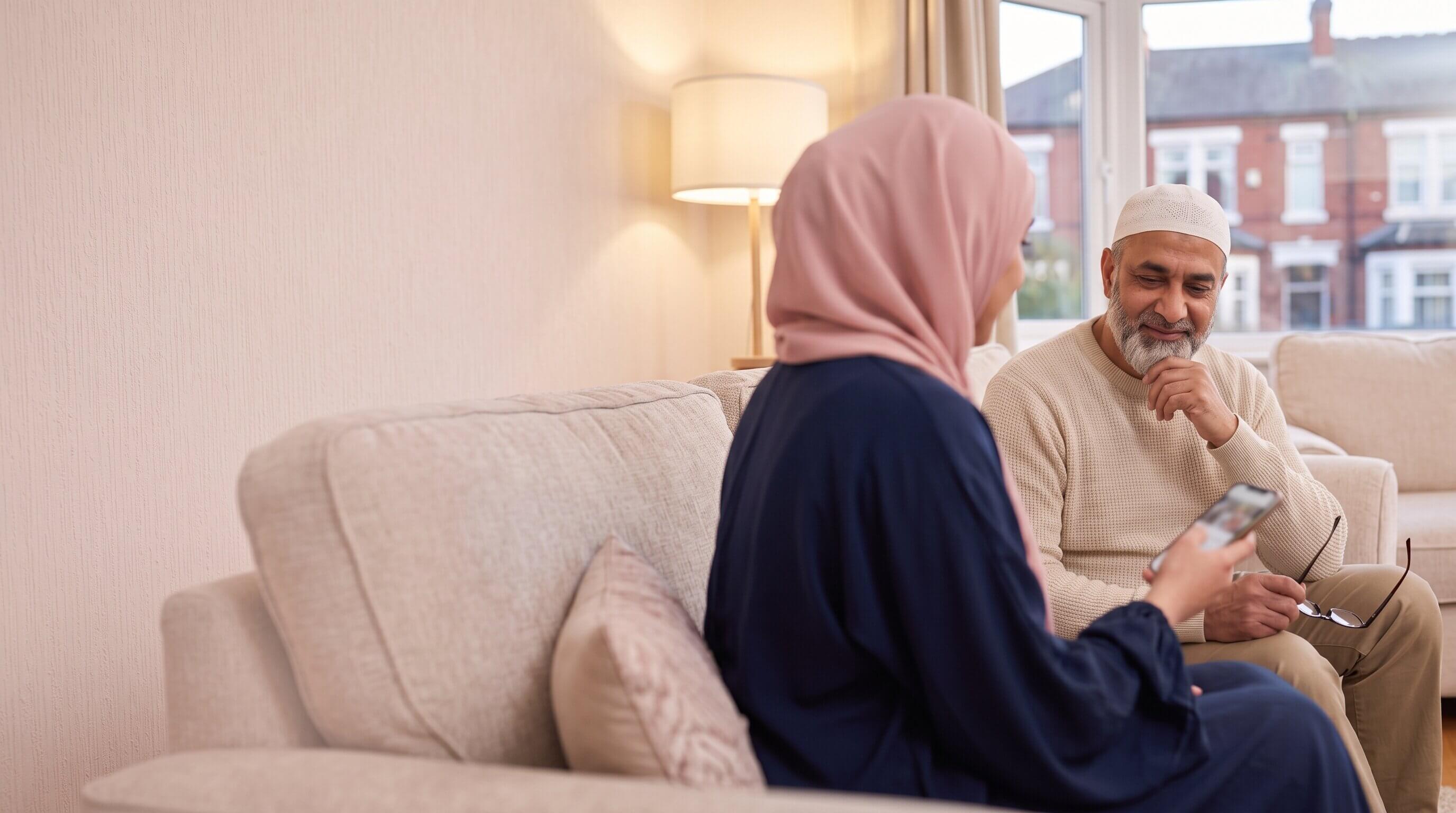 A Muslim woman in a pink hijab talking with her father on the sofa at home