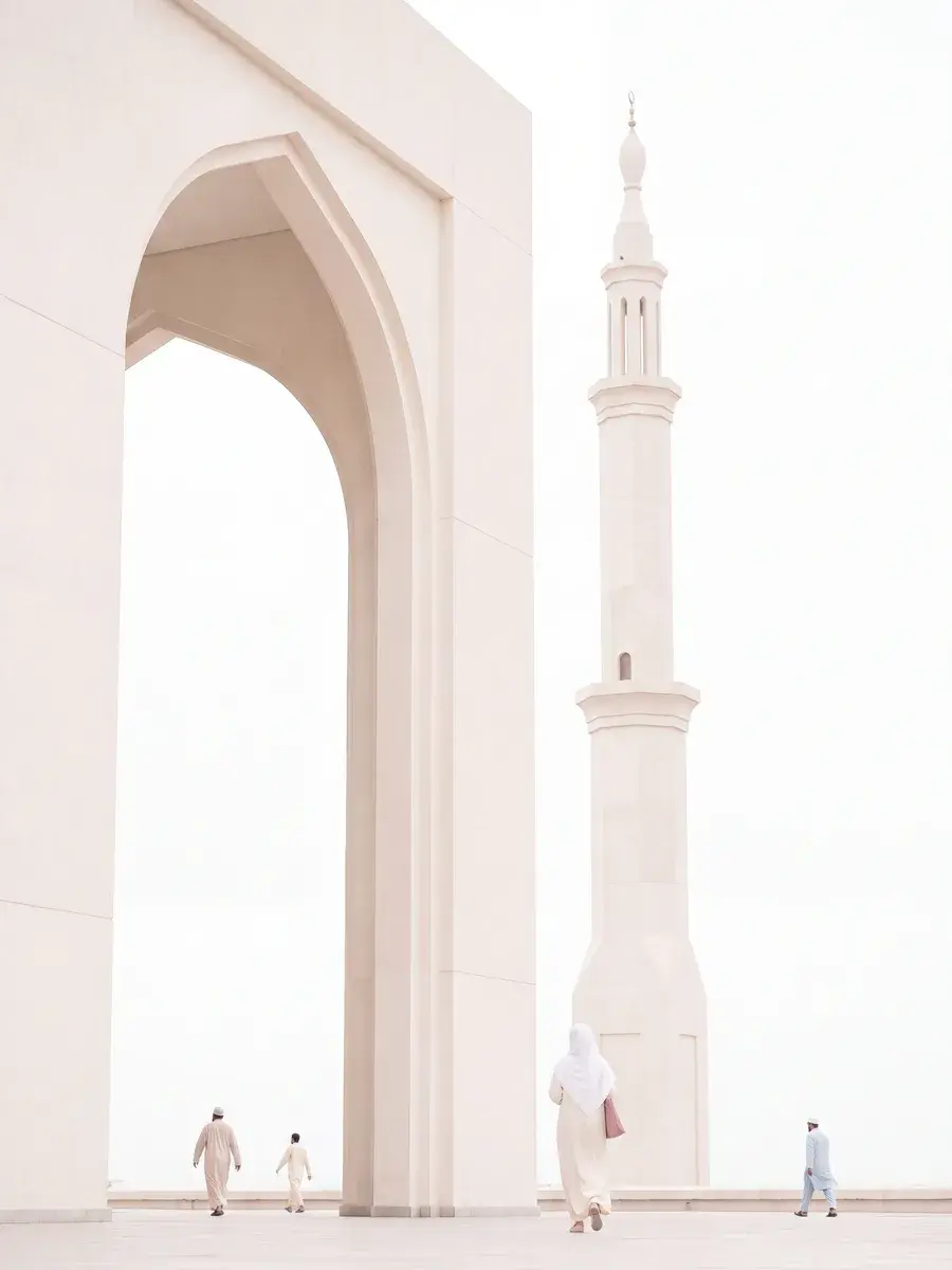 A sunlit white mosque arch and minaret, with figures crossing the courtyard