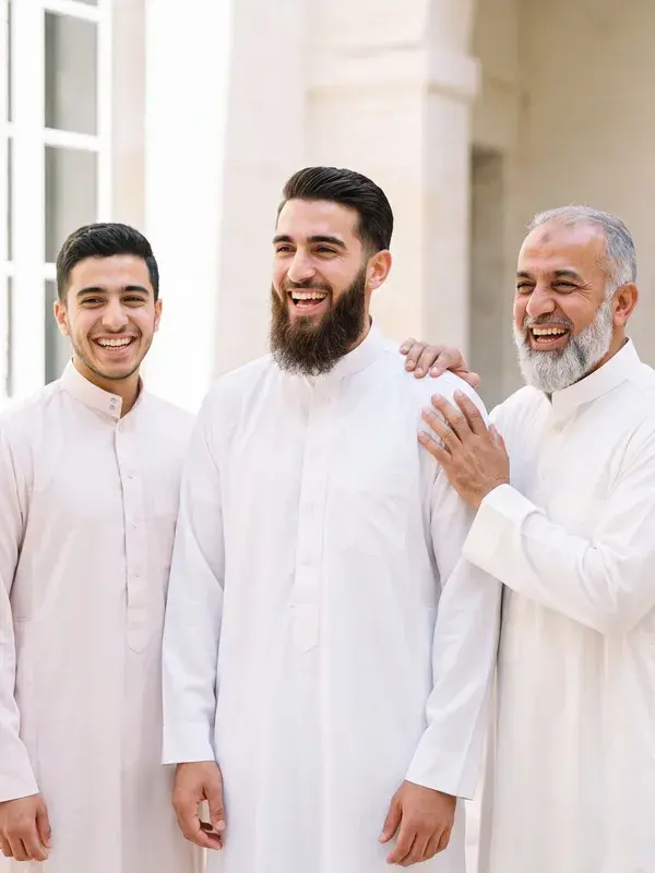 A groom in a white thobe laughing with his father and brother on his wedding day