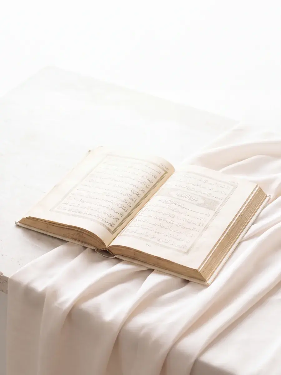 An open Qur'an resting on white silk in daylight